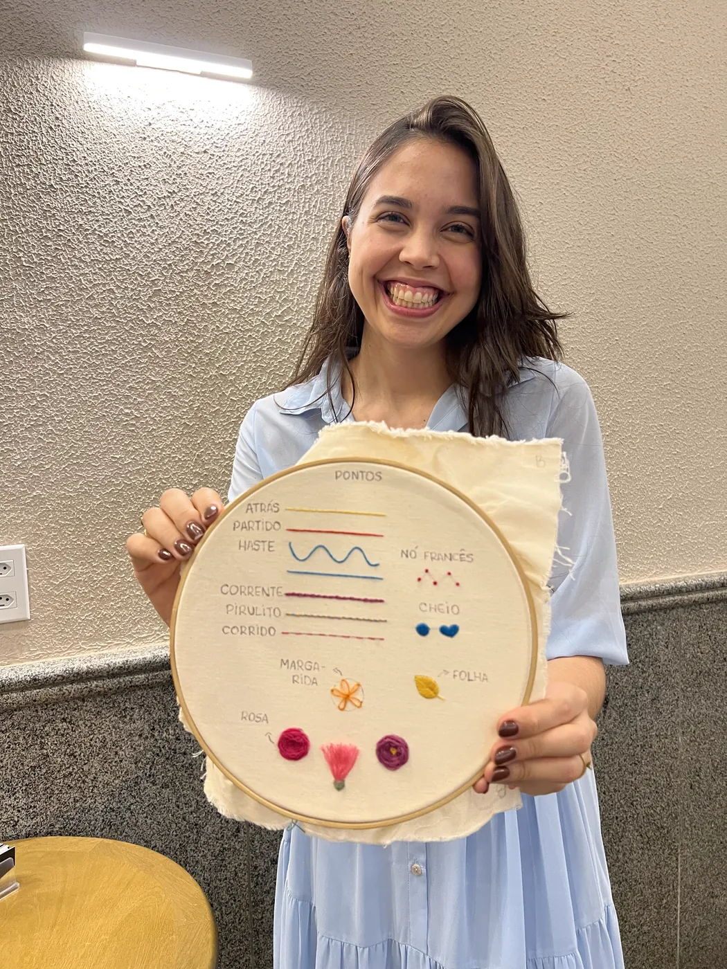 Bárbara com o bastidor da amostra de pontos, no ateliê